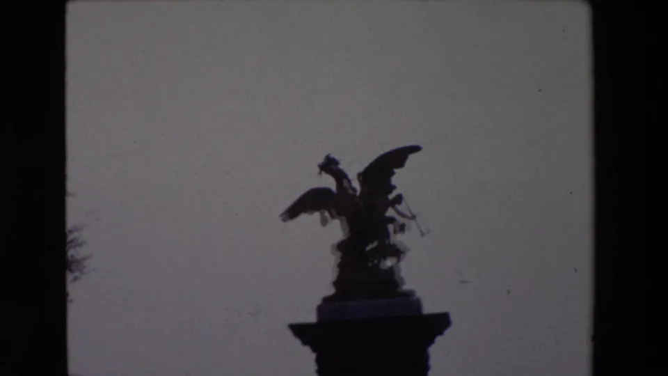 Tight 1969 Paris frame showing the winged statue silhouetted on its pedestal, with little surrounding context beyond the pale sky and faint tree edge.