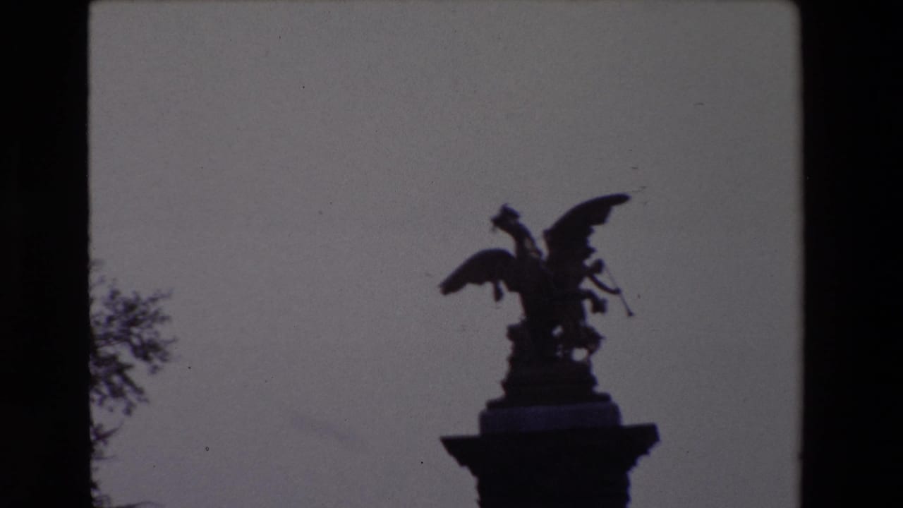 Paris 1969 8mm frame showing a dark silhouetted winged statue atop a column, with tree branches at the edge of the frame.