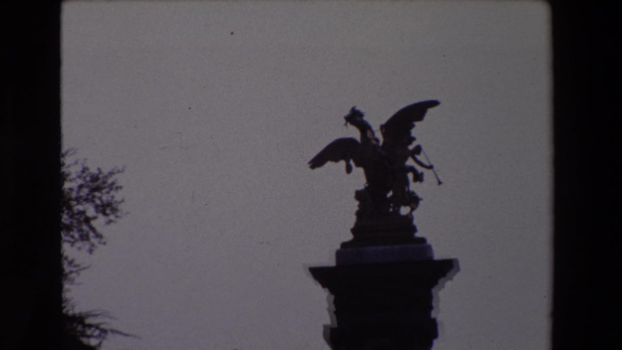 Paris 1969 home-movie frame with the winged statue still silhouetted on its column, framed by sky and partial trees.