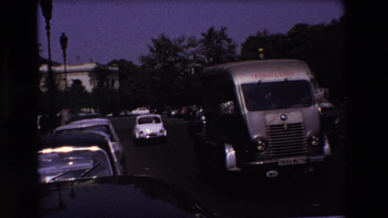 1969 Paris street view with a silver delivery van, parked cars, and compact white vehicles moving through dusk traffic.