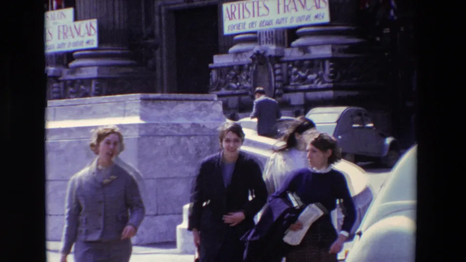 In 1969 Paris street footage, women walk past stone architectural details, parked cars, and a visible Salon des Artistes Francais sign.