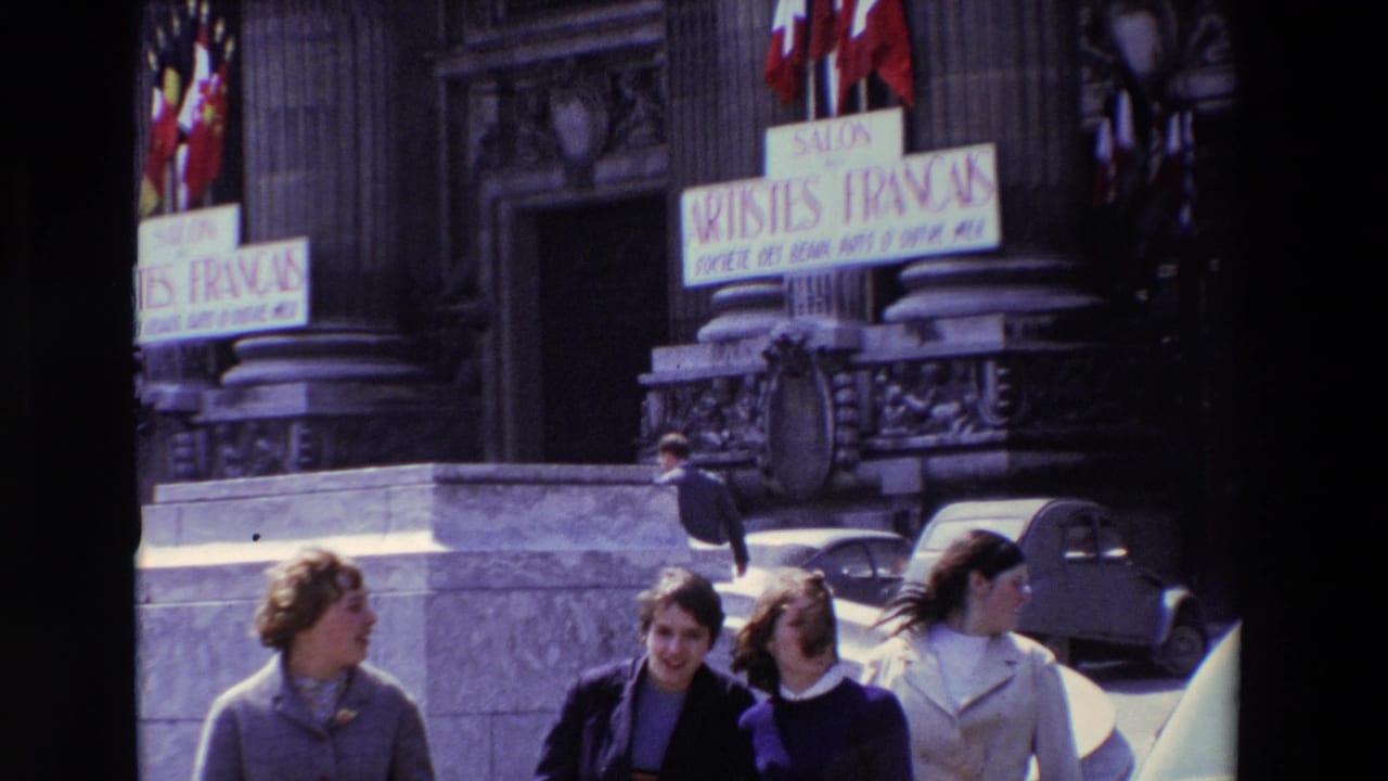 Paris, France in 1969: pedestrians in period clothing walk past the stone entrance of the Salon des Artistes Français, with French flags, signage, steps, and parked cars visible.