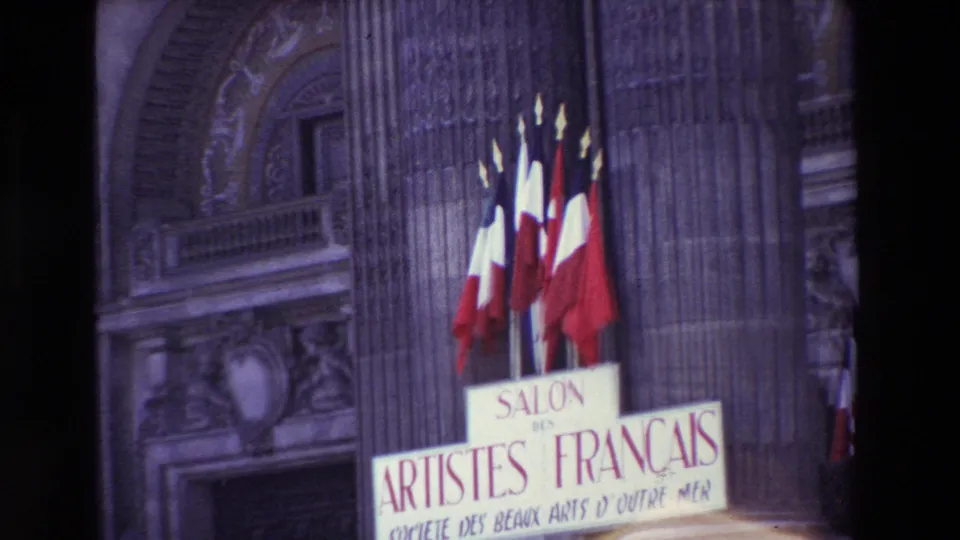 Paris, France in 1969: French flags hang above a Salon des Artistes Français sign on an ornate stone building, with the frame cropped tightly by the handheld 8mm camera.