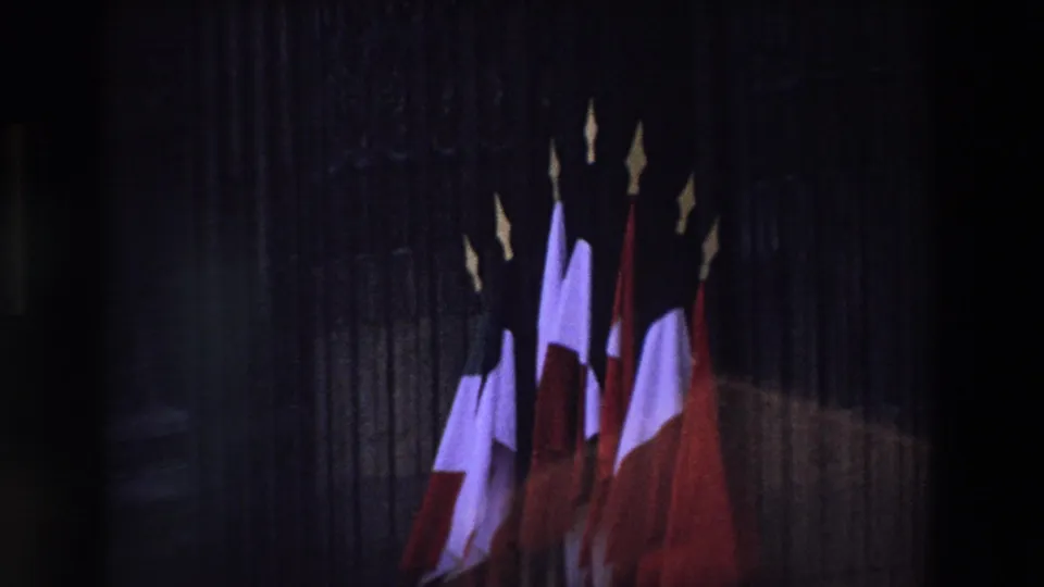 Underexposed 1969 Paris home-movie frame with French tricolor flags partially silhouetted against a stone building facade.