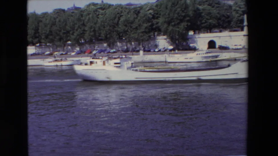 Near the end of the clip, the white river boat passes low across the frame while the Paris embankment, trees, parked cars, and arched wall opening remain visible behind it.