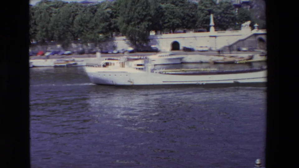 1969 Paris 8mm frame showing the white river vessel lower in the frame as it passes the Seine embankment, with parked cars and a stairway visible above.