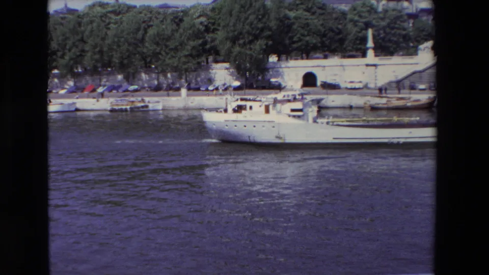 1969 Paris 8mm frame with the white river boat moving toward the edge of the frame, backed by the Seine embankment, trees, cars, and a dark arched opening.