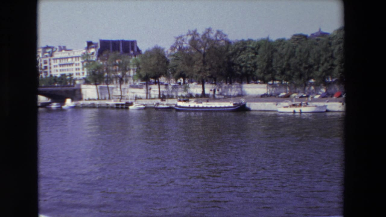 Seine riverbank with several moored boats, parked cars, trees, and buildings.
