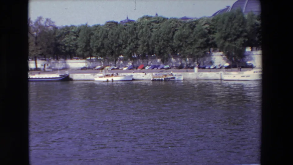 1969 Paris riverbank frame showing moored boats and parked cars below a line of trees, with rippling water filling the lower foreground.