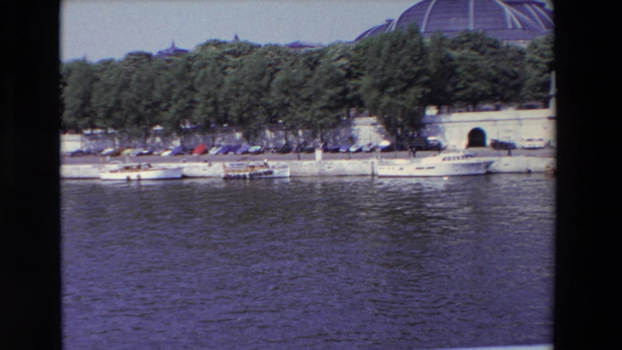 Riverbank with white boats, trees, parked cars, and a tunnel opening.