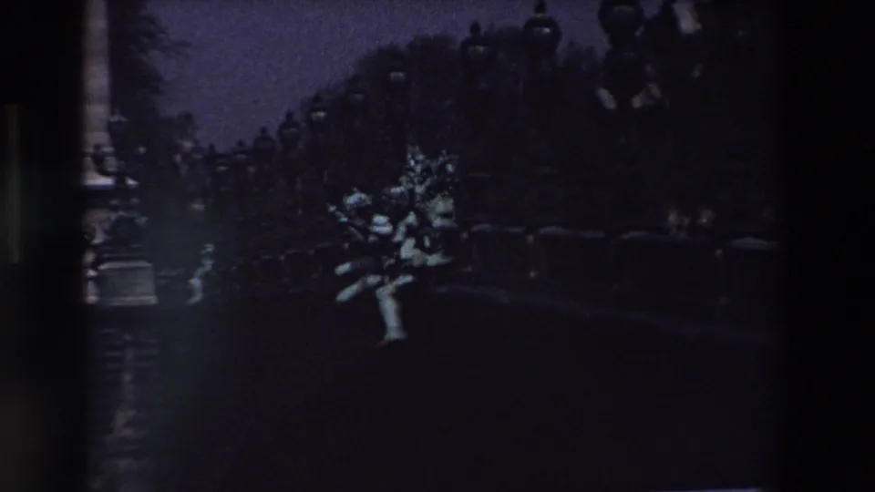 1969 Paris frame with the statue brighter than the surrounding park or boulevard setting, framed by dark foliage, lampposts, and blue dusk exposure.
