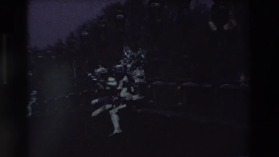 1969 Paris 8mm still showing the pale sculpture from a slightly lower or shifted handheld angle, with dark trees, lamppost forms, and shadowed ground around it.
