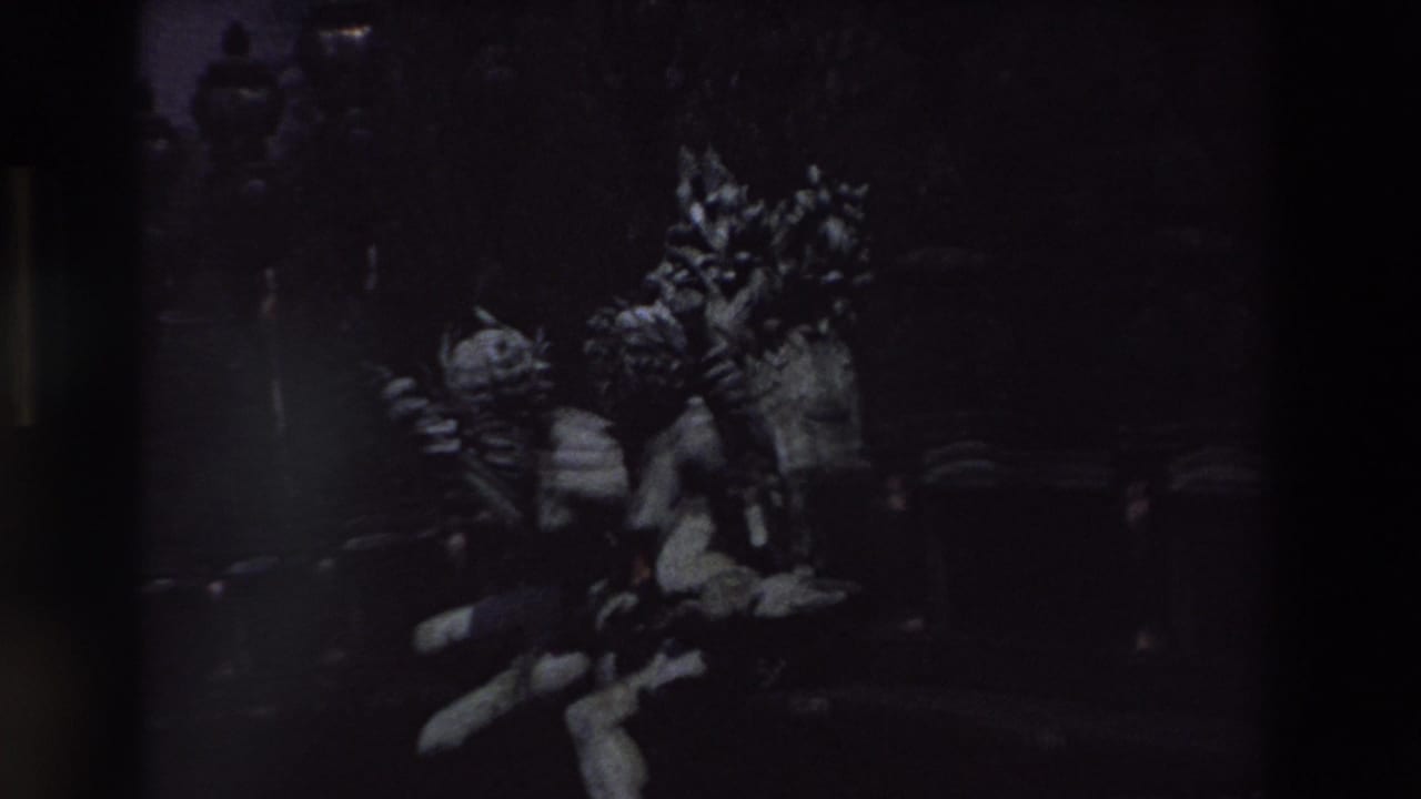Underexposed 1969 Paris home-movie frame showing ornate public sculpture, decorative lamp standards, and stone architectural details in deep shadow.