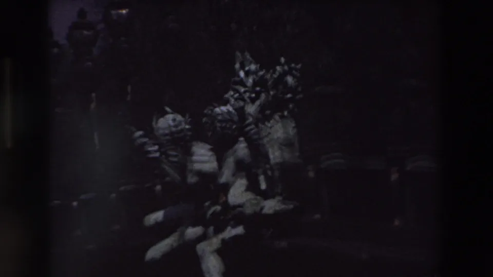 Underexposed 1969 Paris home-movie frame showing ornate public sculpture, decorative lamp standards, and stone architectural details in deep shadow.