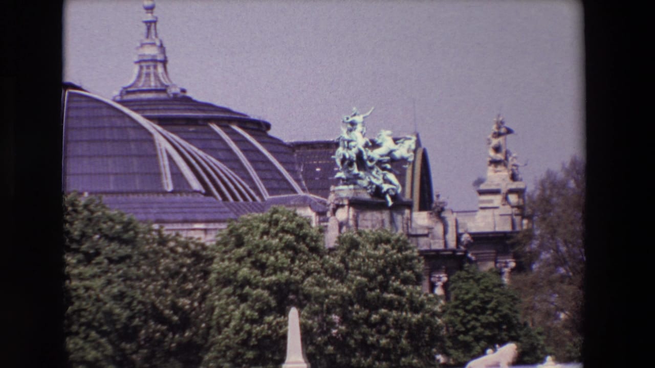 1969 Paris home-movie frame showing a domed landmark exterior behind trees, with a patinated bronze equestrian sculpture and ornate stonework visible above the foliage.