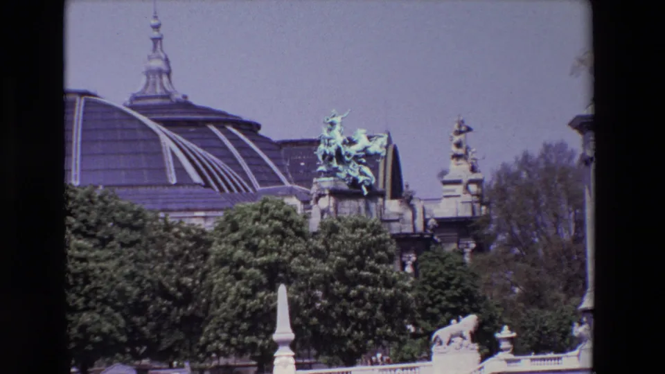 1969 Paris 8mm frame showing a historic domed building with green bronze sculptural figures, heavy foliage, stone details, and garden ornamentation in the foreground.