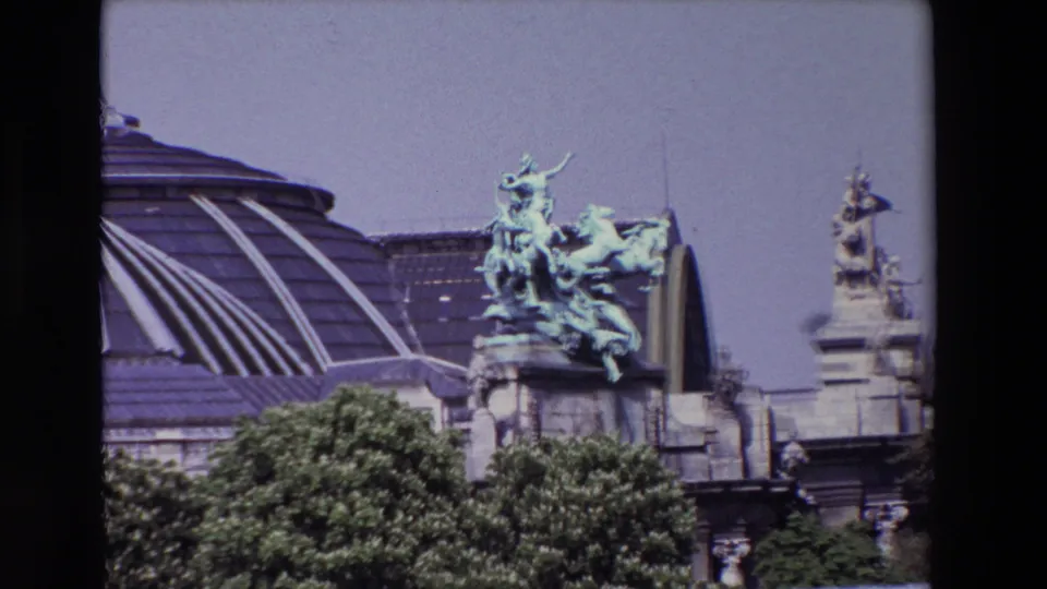 1969 Paris 8mm frame showing a green-patinated equestrian sculpture on a grand stone building, with a glass roof and trees below.
