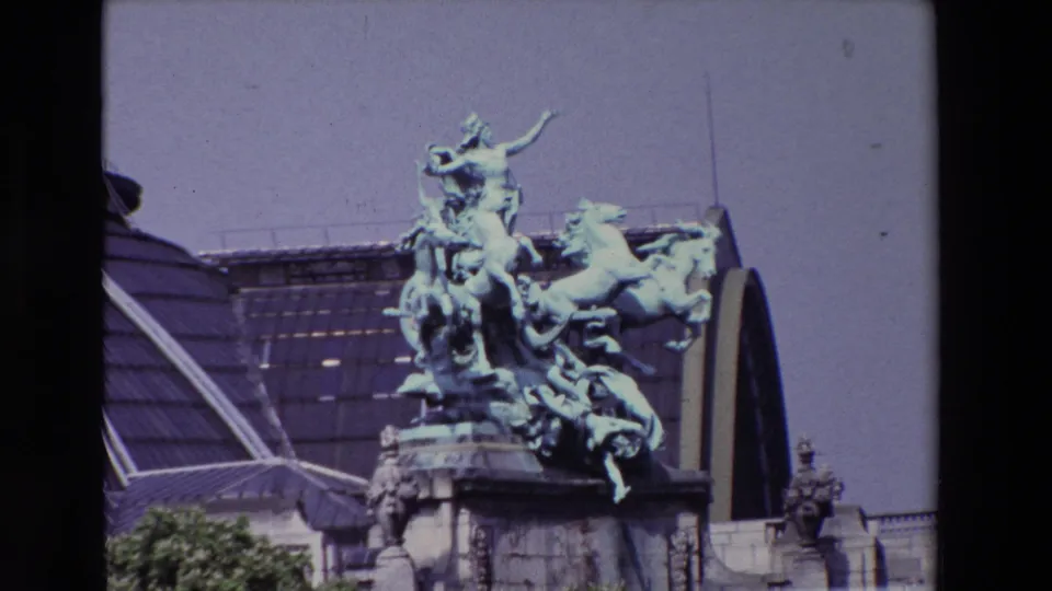 Closer 1969 Paris view of the patinated horse group and figures mounted above a stone facade with an arched glass roof behind it.