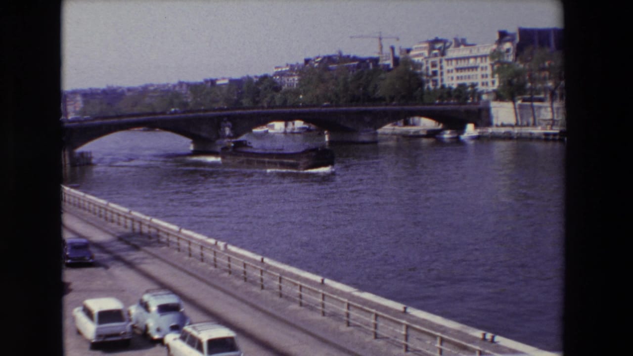 1969 Paris 8mm frame showing a large barge on the Seine near a stone arch bridge, with light-colored cars and a railing in the foreground.
