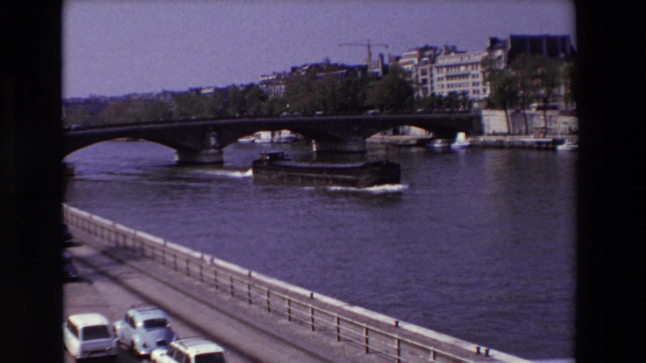 Boat continues along the river near the bridge as cars line the lower road.