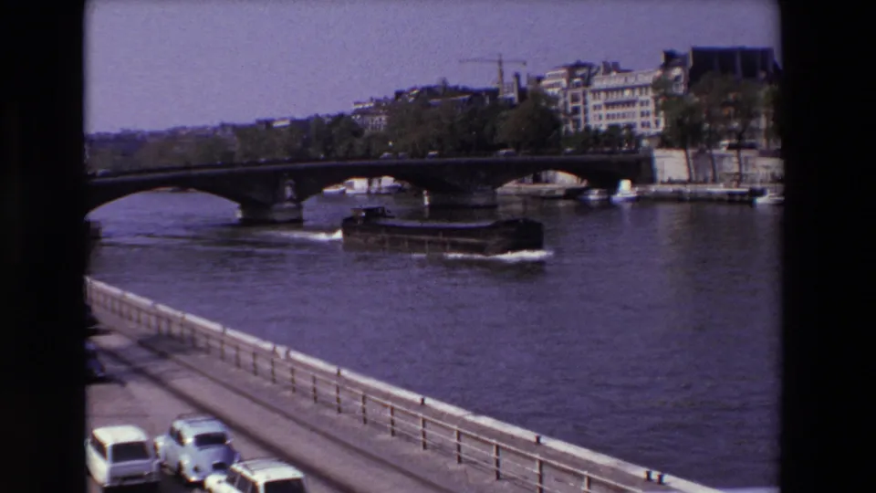 1969 Paris frame with a riverboat moving past a bridge on the Seine, seen from an elevated riverside viewpoint with cars below.