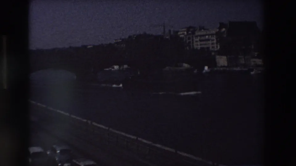 Darkened final 8mm frame of the 1969 Paris Seine scene, with the bridge, river, cars, and distant buildings still faintly visible.