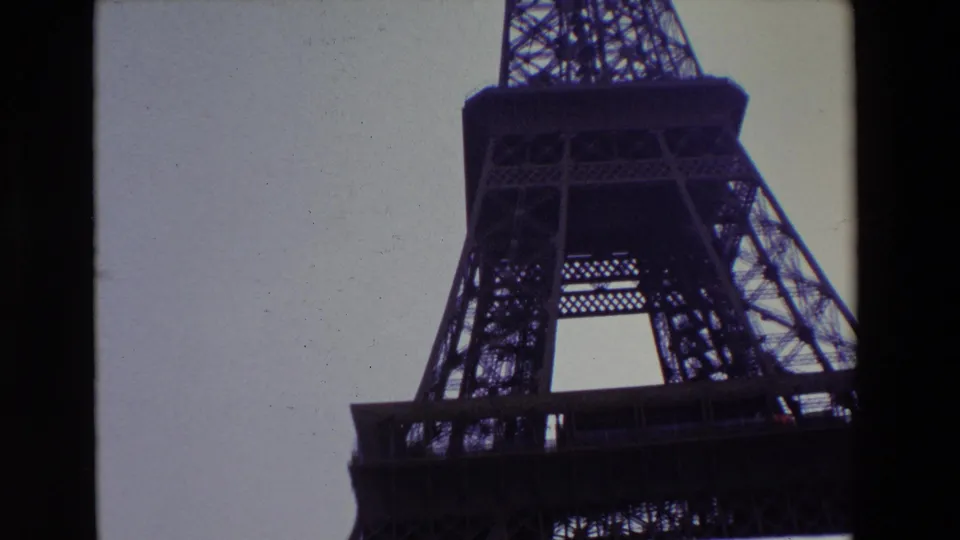 1969 Paris frame looking up at the Eiffel Tower's leg and platform, with the lower arch partly cropped and the soft 8mm image framed by dark borders.