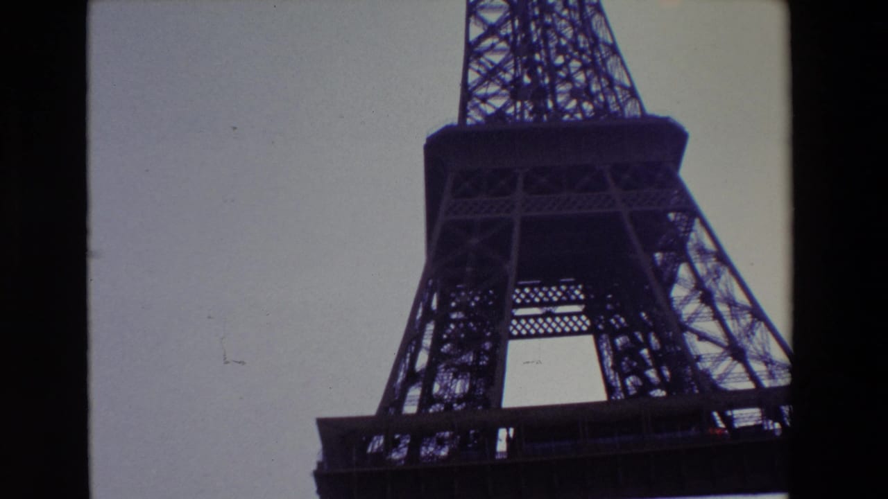 Low-angle view of the Eiffel Tower silhouetted against a pale sky.