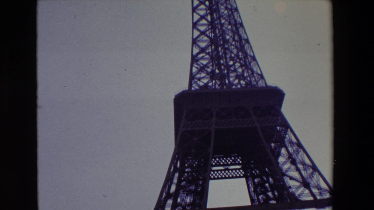 Eiffel Tower structure framed high against a pale sky with dark film borders.