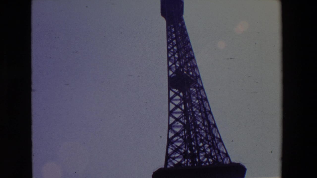 1969 Paris 8mm frame with the Eiffel Tower lattice cropped along the right side, silhouetted against a faded purple-gray sky and bordered by the film gate.