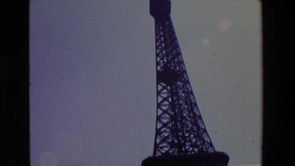 1969 Paris 8mm frame with the Eiffel Tower lattice cropped along the right side, silhouetted against a faded purple-gray sky and bordered by the film gate.