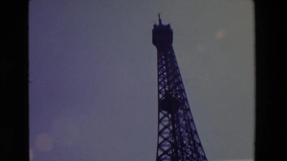 1969 Paris 8mm frame showing the upper Eiffel Tower and spire in silhouette, with muted color, dust marks, and handheld home-movie framing.