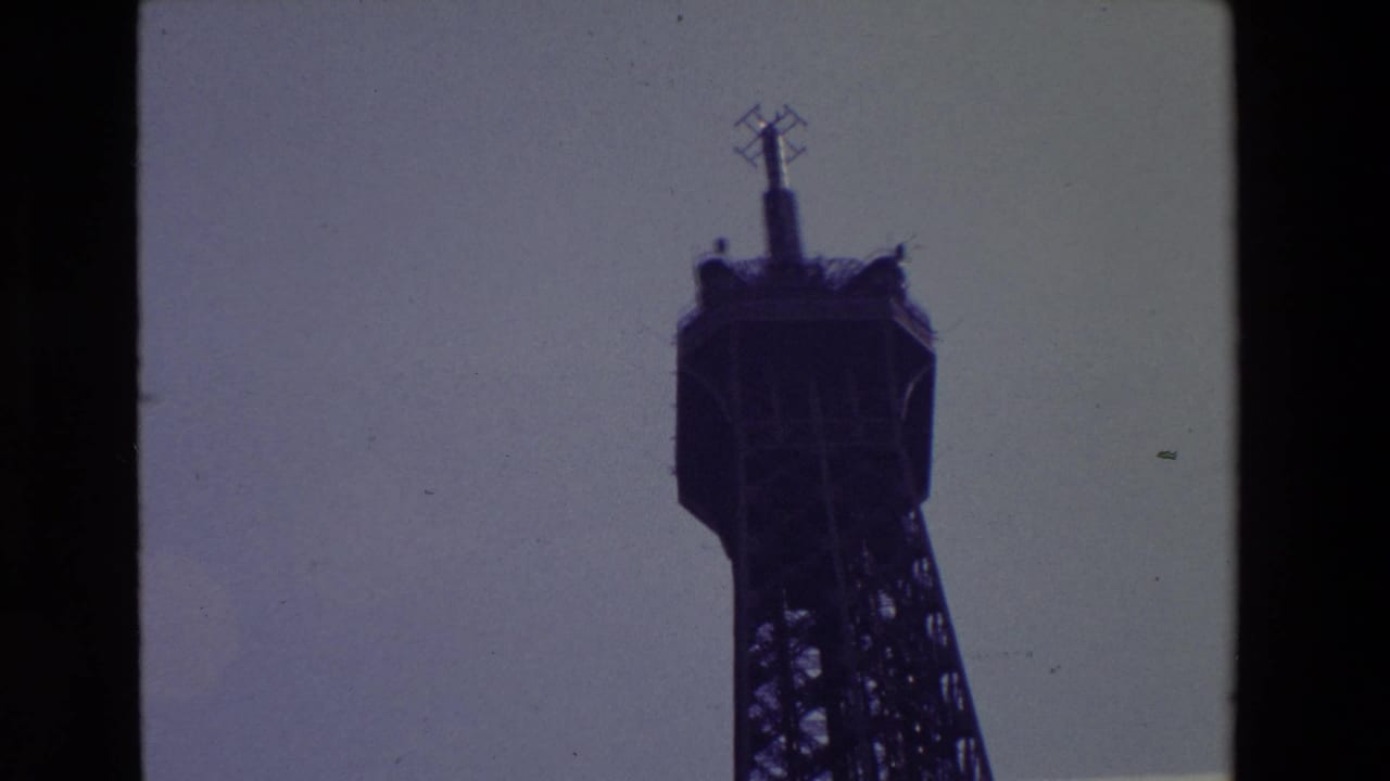 1969 Paris frame with the Eiffel Tower summit silhouetted near the right side, showing the antenna mast and upper lattice detail against open sky.