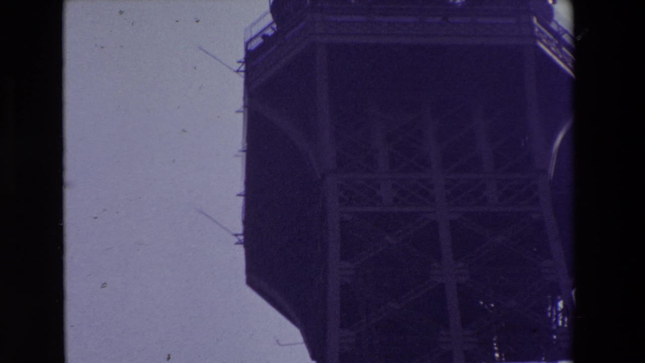 1969 Paris 8mm frame with the Eiffel Tower's upper platform cropped at the edge of the frame, showing underside cross-bracing and antenna elements.