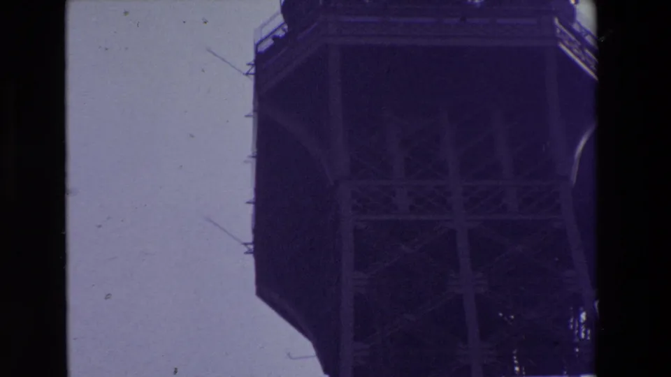 1969 Paris 8mm frame with the Eiffel Tower's upper platform cropped at the edge of the frame, showing underside cross-bracing and antenna elements.