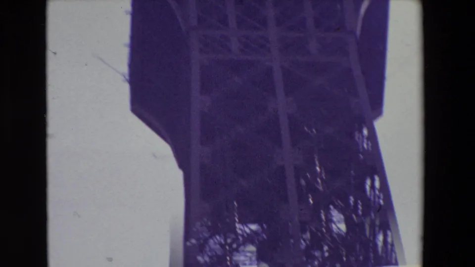 1969 Paris 8mm frame looking up at the Eiffel Tower, with the platform edge, heavy iron supports, and dense latticework filling much of the view.