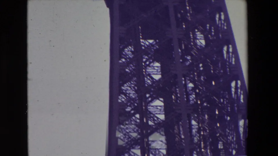 1969 Paris 8mm frame showing the Eiffel Tower's lower upper-section latticework, vertical iron supports, and platform underside from a steep upward angle.