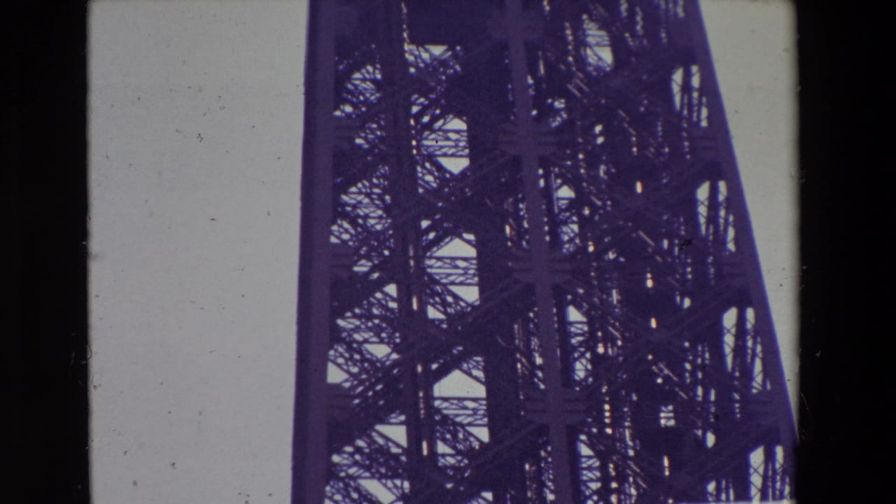1969 Paris home-movie frame looking upward at the Eiffel Tower lattice and support structure, with dark film borders and contact-sheet division visible.