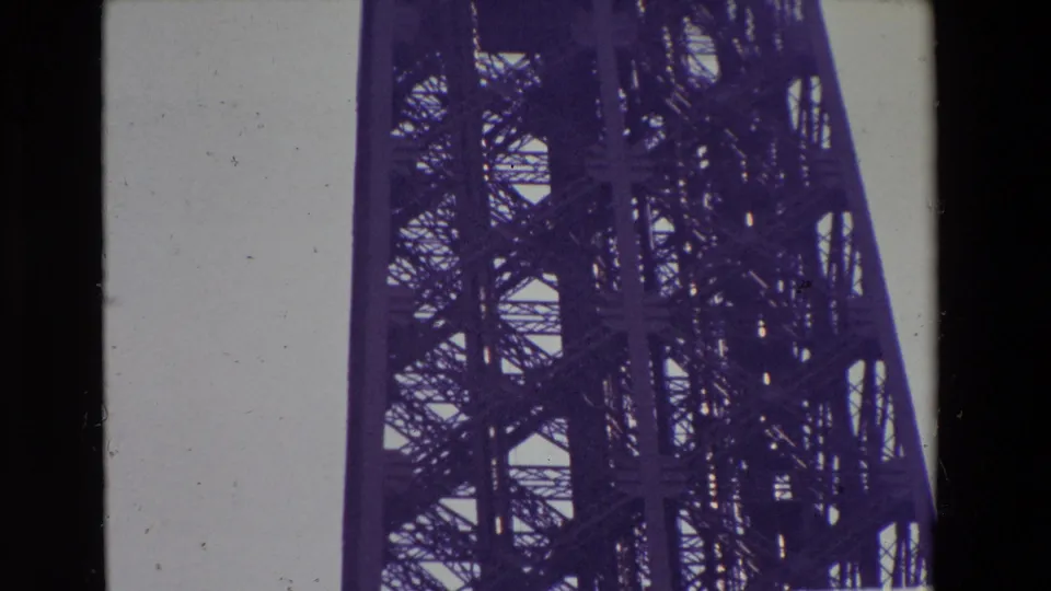 1969 Paris home-movie frame looking upward at the Eiffel Tower lattice and support structure, with dark film borders and contact-sheet division visible.