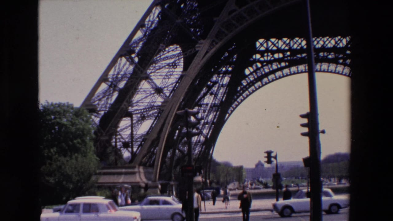 Eiffel Tower arch over a Paris street with cars, pedestrians, trees, and traffic lights.