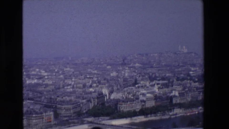 End frame of a 1969 8mm Paris cityscape, with dense buildings beside the Seine and the white domes of Sacré-Cœur visible far in the background.