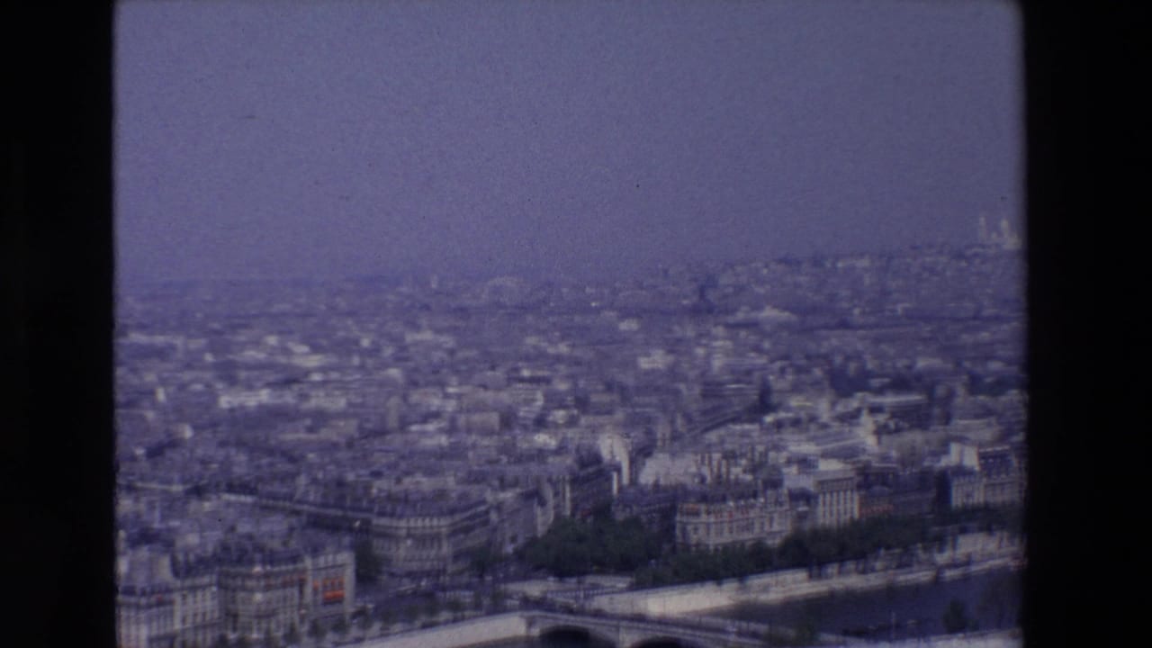 Elevated view over Paris rooftops and the Seine River through a film gate.