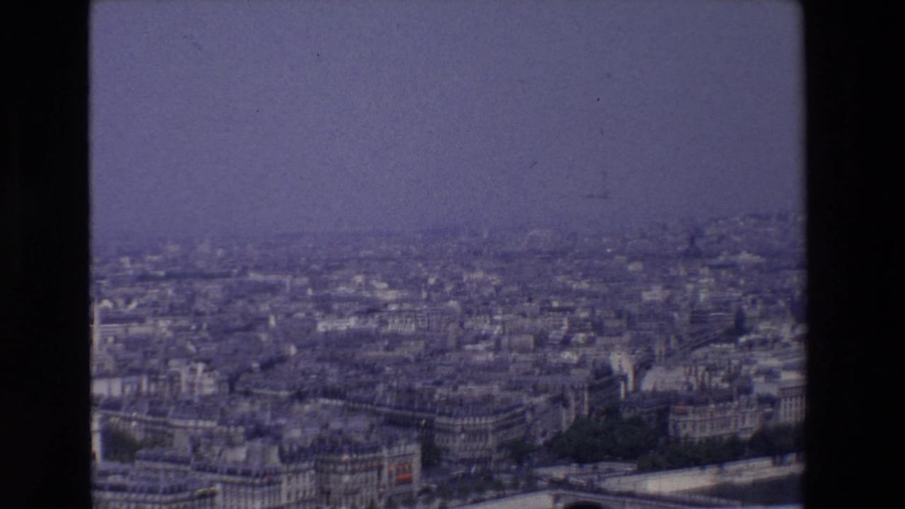 Wide elevated Paris panorama with riverfront buildings and distant skyline haze.