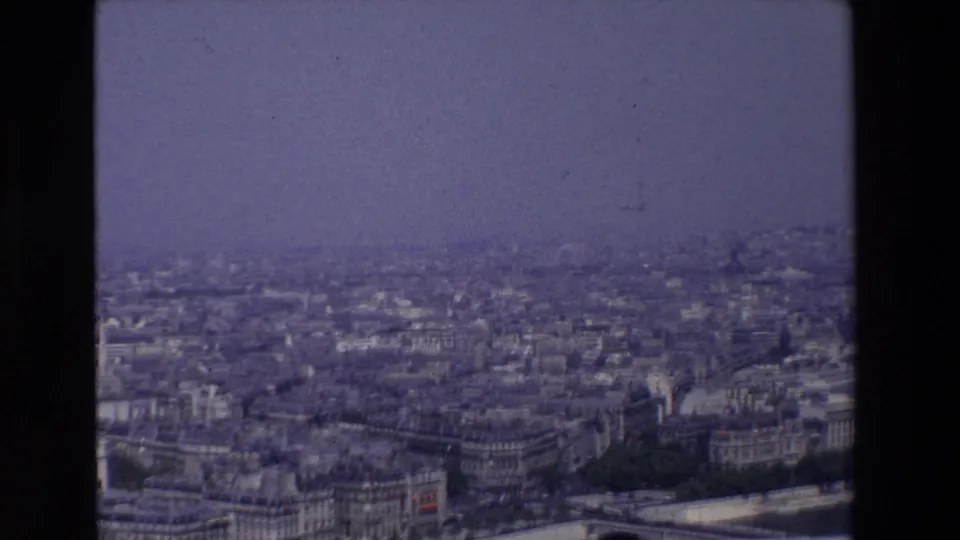 1969 8mm Paris panorama from an elevated vantage, with the Seine corridor, rows of urban buildings, and a soft blue-purple haze across the skyline.