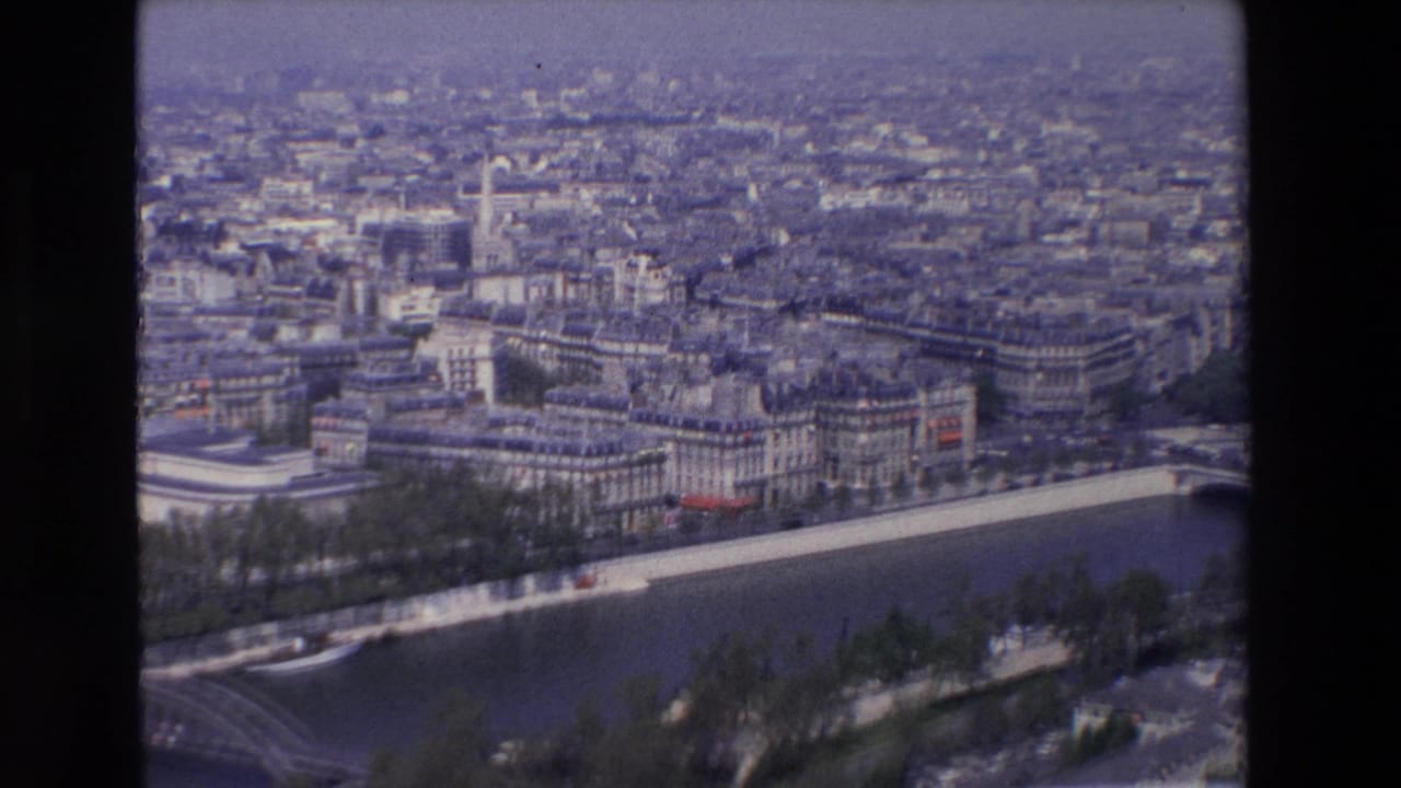 1969 8mm aerial view of Paris showing the Seine River, tree-lined embankments, dense city blocks, and a partial bridge crossing near the lower edge.