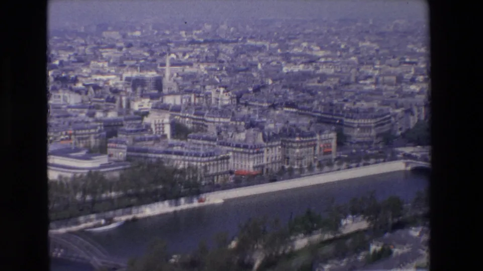 1969 8mm aerial view of Paris showing the Seine River, tree-lined embankments, dense city blocks, and a partial bridge crossing near the lower edge.