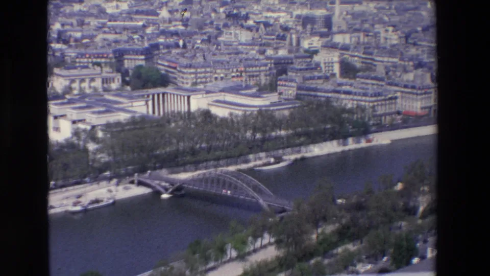 1969 Paris aerial frame showing the Seine, an arched metal bridge, riverside traffic lanes, rows of trees, and surrounding city architecture.