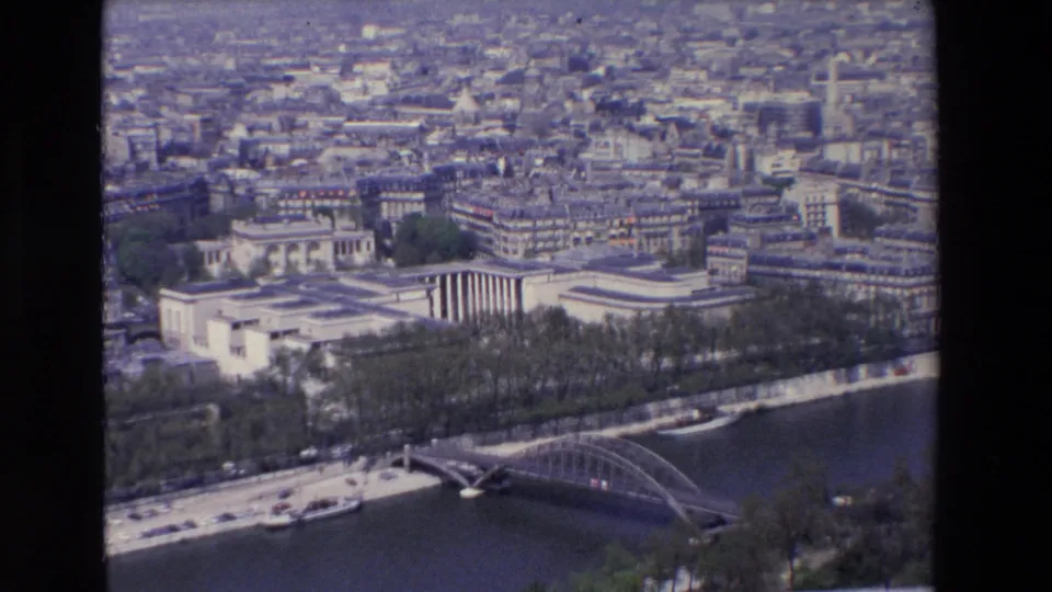 1969 aerial view of Paris with the Seine in the foreground, a bridge crossing the river, tree-lined embankments, and dense city blocks stretching into the distance.