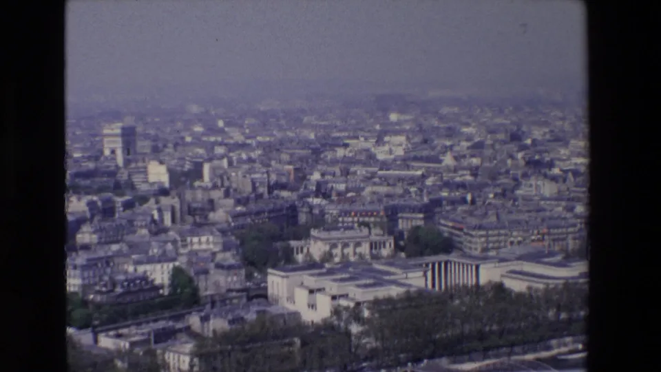 1969 8mm view over Paris rooftops and avenues, with the Arc de Triomphe visible in the distance beneath a hazy overcast sky.