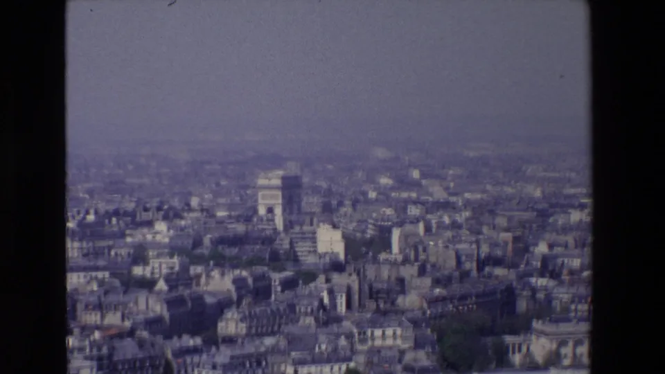 1969 home-movie frame looking across Paris from above, with the Arc de Triomphe, compact rooflines, and muted blue-gray haze visible.